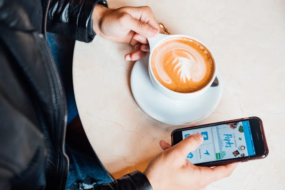 A person comparing dating apps on a smartphone over coffee.